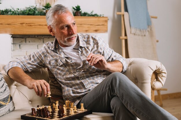 Gros plan, homme aîné, s&#39;asseoir sofa, jouer échecs