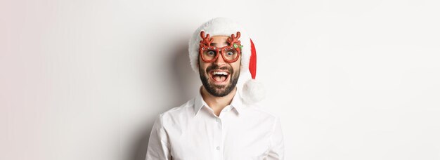 Gros plan d'un homme barbu excité dans des lunettes de noël et un bonnet de noel à la surprise de l'offre promotionnelle wint