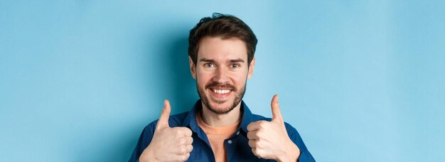 Gros plan d'un homme beau et souriant montrant les pouces vers le haut louant le bon travail recommandant la position de l'entreprise