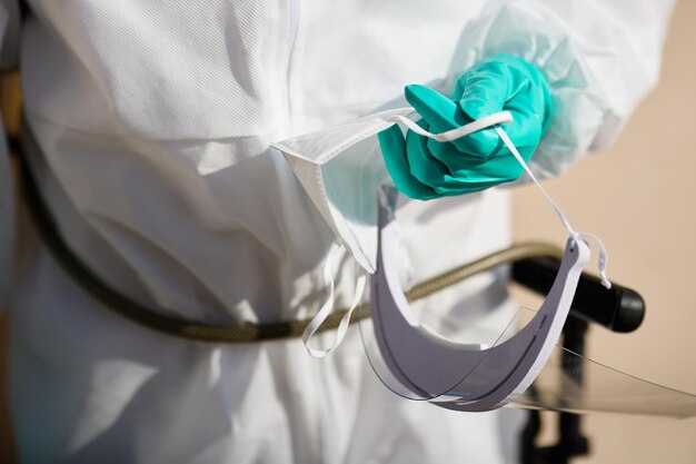 Gros plan d'un homme en costume de matières dangereuses tenant une visière et un masque de protection