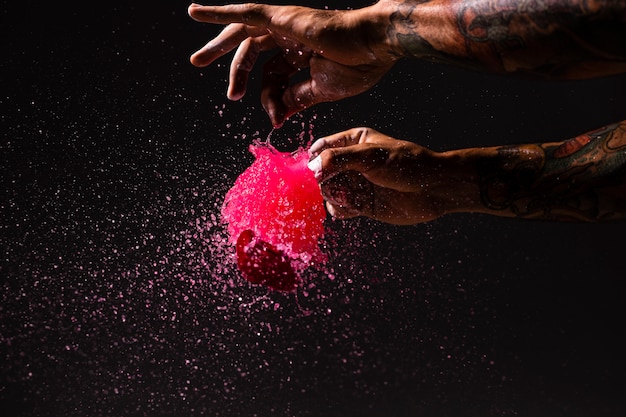 Gros plan homme éclater un ballon avec de la peinture rouge