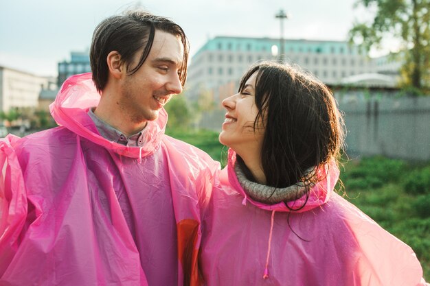 Gros plan d'un homme et d'une femme en imperméable en plastique rose souriant l'un à l'autre de façon romantique