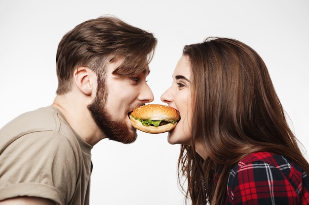 Gros plan de l'homme et la femme mangeant un hamburger ensemble.