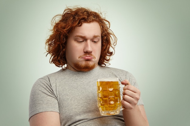 Gros plan d'un homme indécis avec des cheveux roux tenant un verre de bière dans ses mains