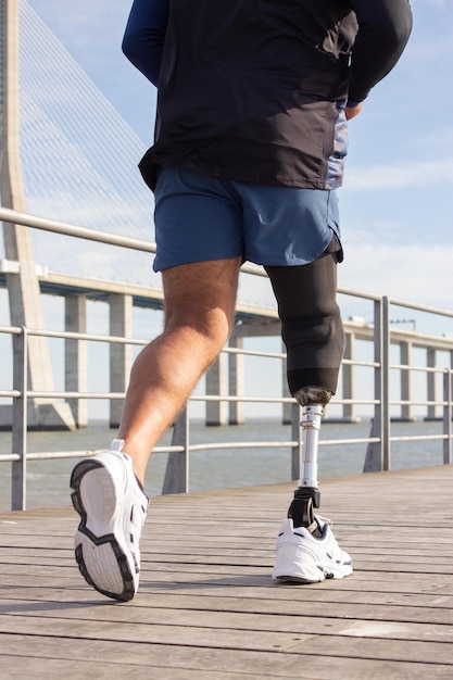 Gros plan sur un homme avec une jambe mécanique en marche. Sportif en short bleu et baskets blanches photographié pendant le jogging. Sport, passe-temps, concept de handicap