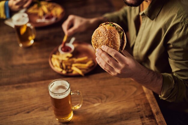 Gros plan sur un homme mangeant un hamburger et des frites au pub