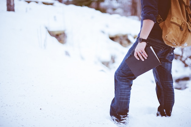 Photo gratuite gros plan d'un homme portant un sac à dos debout dans la neige et tenant la bible