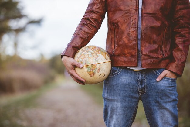 Gros plan d'un homme portant une veste en cuir tenant un globe de bureau avec un arrière-plan flou