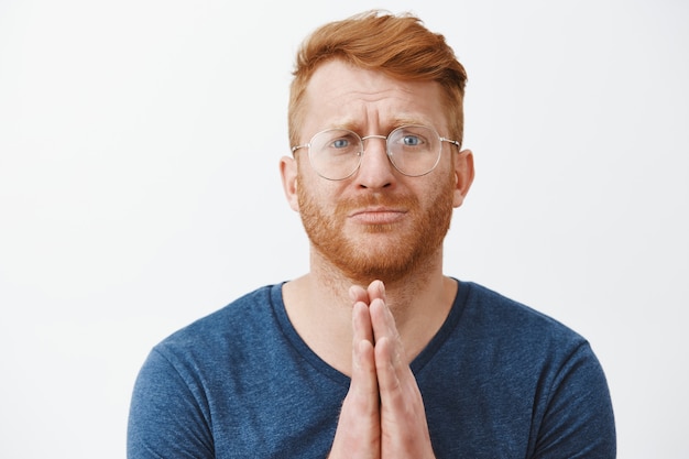 Gros plan d'un homme rousse suppliant plein d'espoir à lunettes a besoin d'aide, vous suppliant