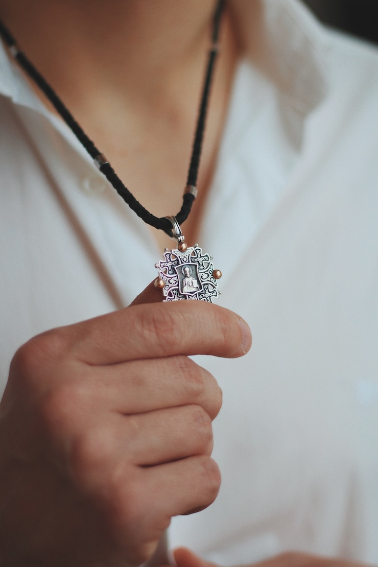 Photo gratuit gros plan d'un homme tenant un collier à breloques avec un pendentif en argent et un cordon noir