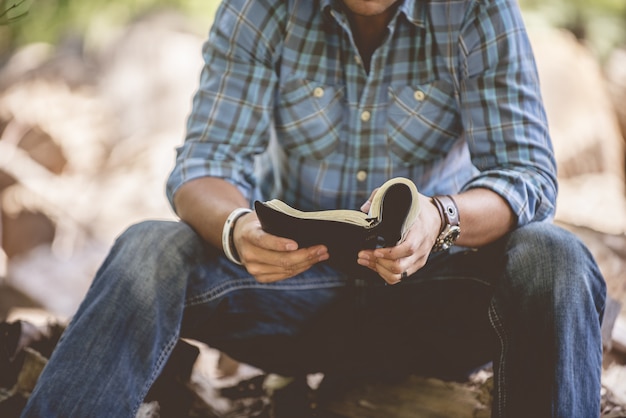 Gros plan d'un homme en vêtements décontractés lisant la Sainte Bible sur un arrière-plan flou