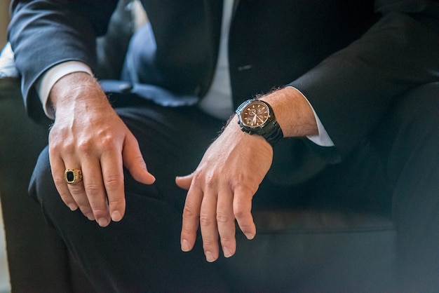 Gros plan d'un homme vêtu d'un costume, plus précisément: ses mains, sa bague et sa montre-bracelet
