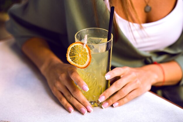 Gros plan image de détails de femme tenant un cocktail de limonade savoureux frais, belles mains avec manucure française, vêtements élégants décontractés, couleurs toniques.