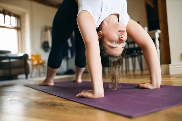 Photo gratuite gros plan de l'image d'une jeune yogi pratiquant le yoga avancé à la maison, faisant une pose d'arc ou de roue vers le haut, flexion en arrière, gardant les mains et les pieds sur un tapis, étirant la colonne vertébrale et ouvrant la poitrine.