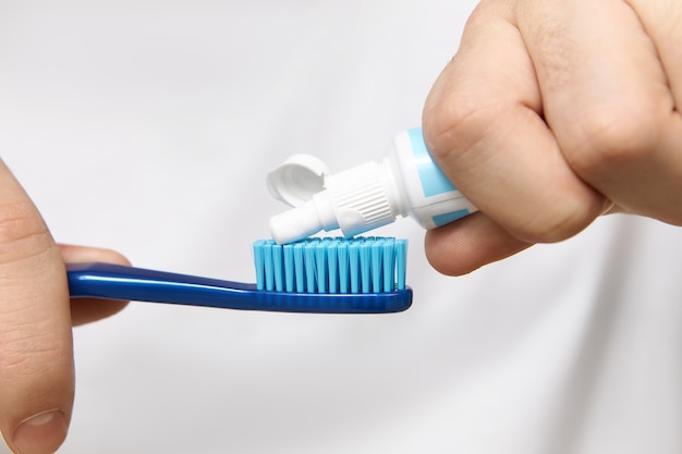 Gros plan image des mains de l'homme tenant le tube, serrant le dentifrice blanchissant sur la brosse.