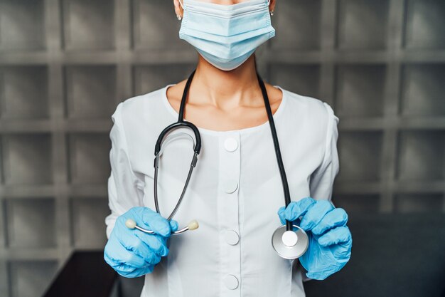 Gros plan d'une infirmière en masque de protection, avec stéthoscope et gants de protection.