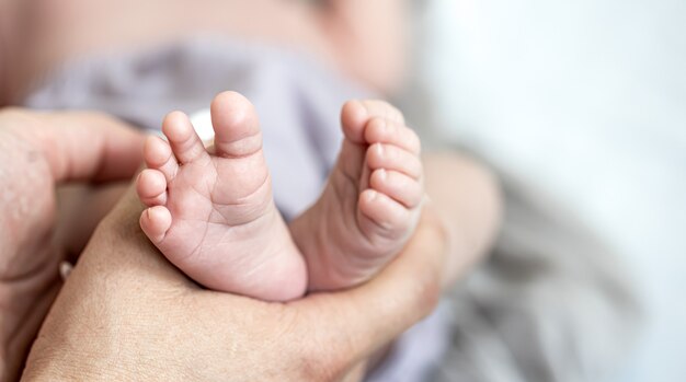 Gros plan des jambes du nouveau-né dans les mains de maman sur fond flou.