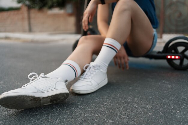 Gros plan des jambes de fille assise sur son scooter électrique en été dans la rue