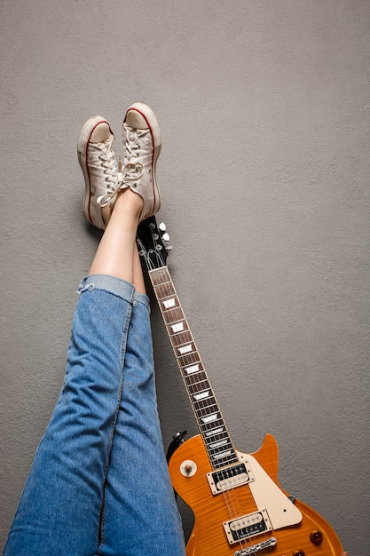 Gros plan des jambes de la jeune fille et de la guitare sur fond gris.