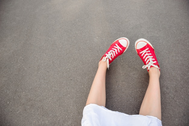 Gros plan des jambes en rouge keds couché sur l'asphalte.