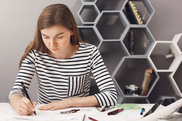 Gros plan de jeune concentré beau jeune designer assis à table dans la salle lumineuse, faisant des plans à l'aide d'un stylo et d'une règle. Concept d'entreprise