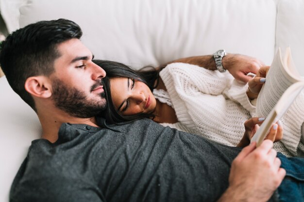 Gros plan, de, jeune couple, coucher, sur, sofa, livre lecture