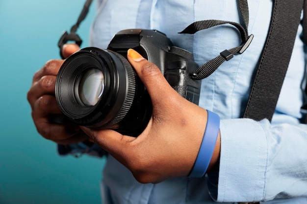 Gros Plan D'une Jeune Femme Adulte Afro-américaine Ayant Un Appareil Dslr Moderne En Se Tenant Debout Sur Fond Bleu. Photographe Professionnel Avec Appareil Photo Se Prépare Pour La Séance De Prise De Vue.