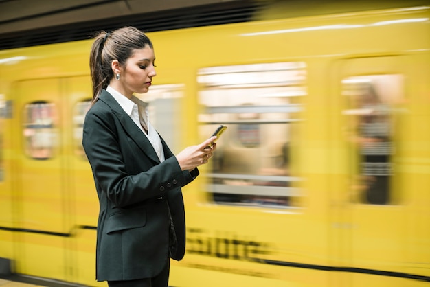 Gros plan d&#39;une jeune femme d&#39;affaires à l&#39;aide de téléphone portable à la station de métro