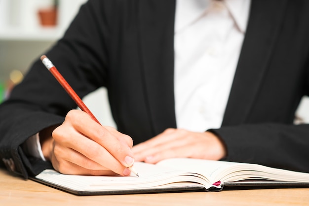 Gros plan, jeune, femme affaires, écrire, crayon rouge, journal