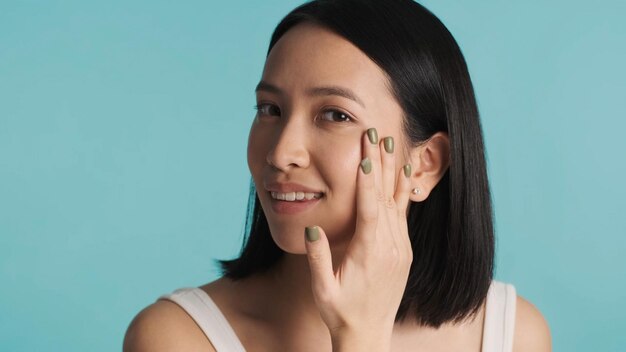 Gros plan d'une jeune femme asiatique appliquant une crème hydratante sur son visage Femme mettant de la crème cosmétique sur son visage en regardant la caméra