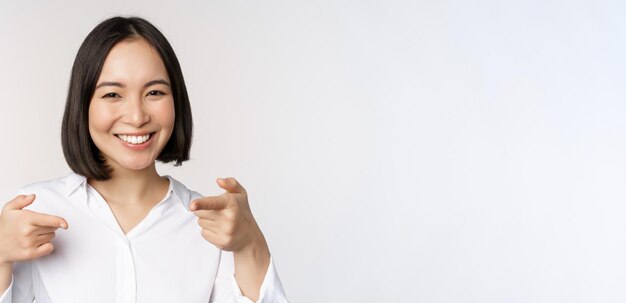 Gros plan d'une jeune femme enthousiaste souriante pointant du doigt la caméra en vous choisissant d'inviter et de recruter des personnes debout sur fond blanc