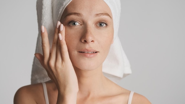 Gros plan jeune femme avec une peau lisse et une serviette sur la tête regardant sensuellement à huis clos sur fond blanc