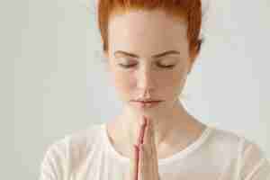 Photo gratuite gros plan d'une jeune femme religieuse au gingembre en chemisier blanc méditant ou priant en gardant les yeux fermés et les mains pressées ensemble, espérant le meilleur. personnes, religion, spiritualité, prière