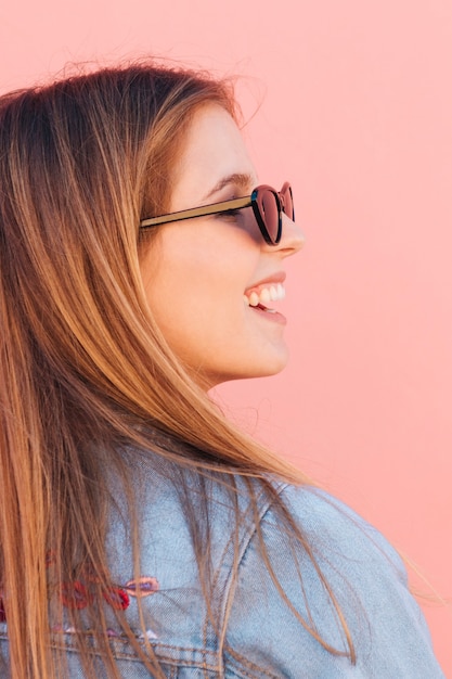 Photo gratuite gros plan d'une jeune femme souriante, lunettes de soleil sur fond rose