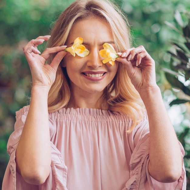 Gros plan d'une jeune femme souriante qui couvre ses yeux avec du freesia jaune