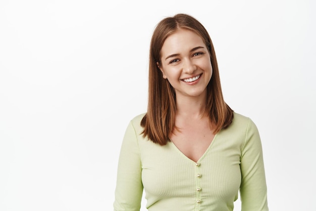 Gros plan d'une jeune fille agréable, souriante et à l'air amicale, heureuse expression du visage mignon, sourire des dents blanches, debout dans un chemisier décontracté sur fond blanc.