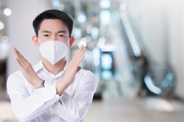 Gros plan jeune homme d'affaires asiatique portant un masque de pollution avec une croix d'action gestuelle pour dire non fond blanc