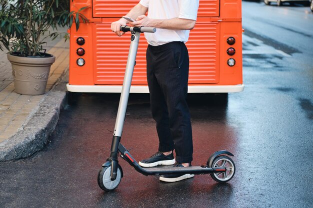 Gros plan jeune homme debout avec un scooter électrique et un téléphone portable avec une camionnette rouge sur fond de rue de la ville