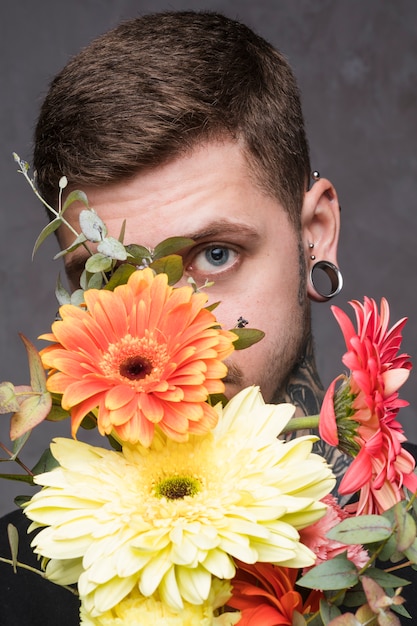 Photo gratuite gros plan d'un jeune homme percé furtivement du bouquet de gerbera