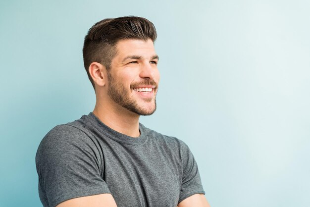 Gros plan d'un jeune homme souriant regardant loin en se tenant debout sur fond turquoise