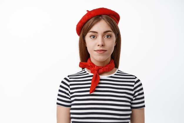 Gros plan d'une jeune mannequin en t-shirt rayé béret français sourit et regarde la caméra avec un visage heureux déterminé se dresse sur fond blanc