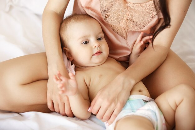 Gros plan de la jeune mère en vêtements de nuit et son nouveau-né allongé sur le lit le matin.