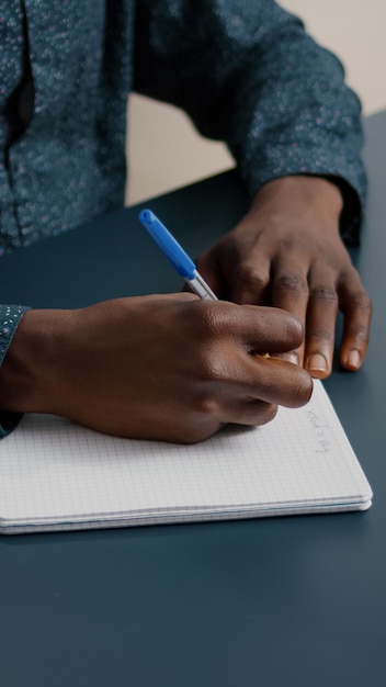 Photo gratuite gros plan sur une jeune personne prenant des notes sur le bloc-notes à l'aide d'un stylo