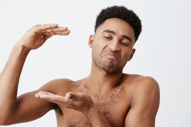 Photo gratuite gros plan de jeunes hommes drôles à la peau noire avec des cheveux bouclés sans vêtements gesticulant avec les mains, montrant une grande taille, regardant de côté avec une expression cynique.