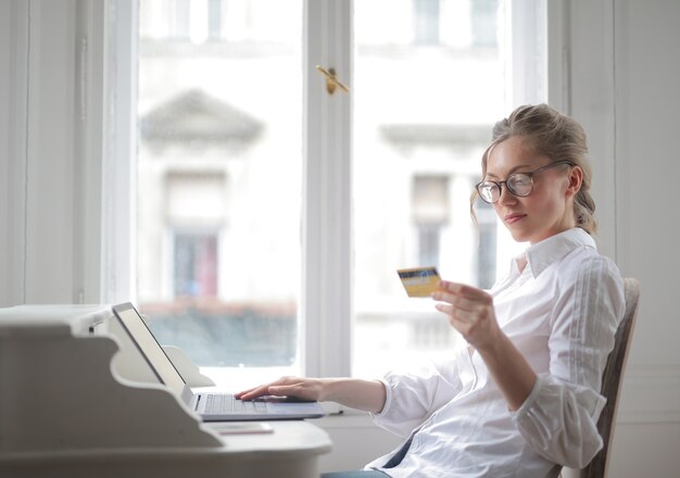 Gros plan de jolie femme avec chemise blanche travaillant avec un ordinateur portable et regardant sa carte