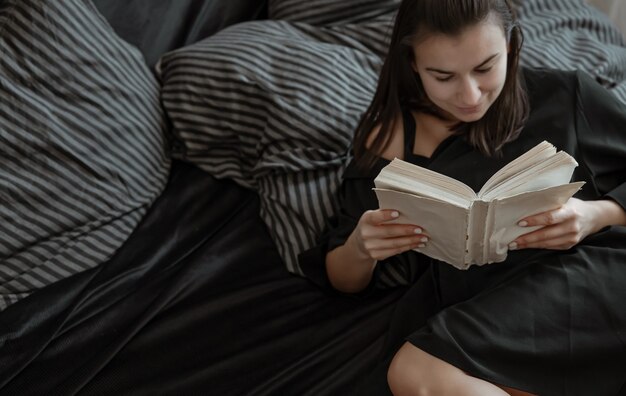 Gros plan d'une jolie femme lisant un livre en position couchée dans un lit douillet.