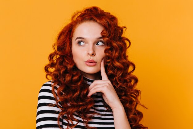 Gros plan d'une jolie fille en T-shirt rayé regardant pensivement à côté contre l'espace orange.
