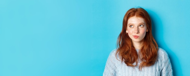 Photo gratuite gros plan d'une jolie rousse pensant et regardant à gauche a une idée debout sur fond bleu