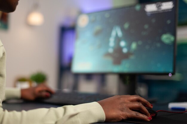 Gros plan sur un joueur professionnel à succès tenant la main sur une souris d'ordinateur jouant à des jeux vidéo de tir spatial pendant le championnat en ligne. Femme joueuse professionnelle utilisant un équipement de jeu RVB en home studio