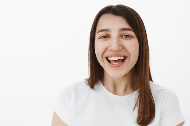 Gros plan d'une joyeuse brune européenne heureuse avec un sourire blanc parfait riant sincèrement à haute voix et regardant joyeux, ravi de s'amuser lors d'un événement hilarant sur un mur gris